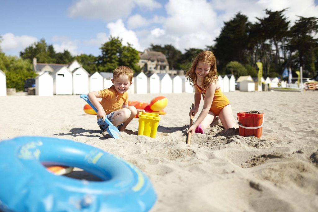 Plage de Port Manec'h, Névez, les enfants sur la plage construisent des châteaux de sable, les cabines en bois blancs en arrière plan. Office de Tourisme de Concarneau à Pont-Aven, Crédit Alexandre Lamoureux